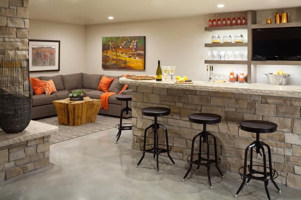 Basement bar and lounge with a stone-faced bar, bar stools, orange sectional and wall-mounted TV