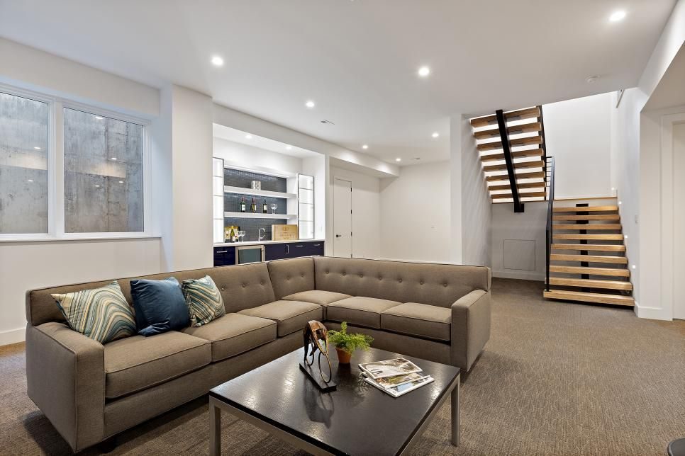 Finished basement lounge with a grey sectional, floating wood staircase and custom built-ins